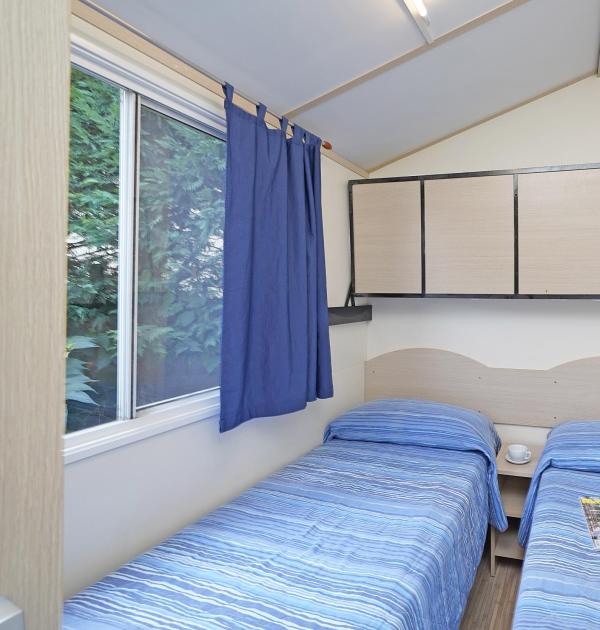 Zimmer mit zwei Einzelbetten, blauen Vorhängen und Schrank.
