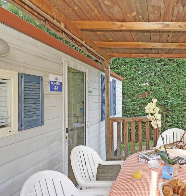 Terrasse mit gedecktem Tisch, weißen Stühlen und Holzdach.