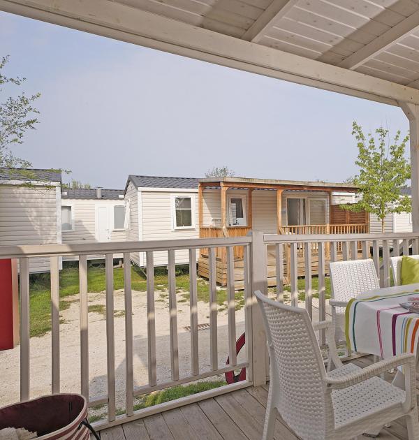 Veranda met tafel, stoelen en uitzicht op stacaravans op een camping.