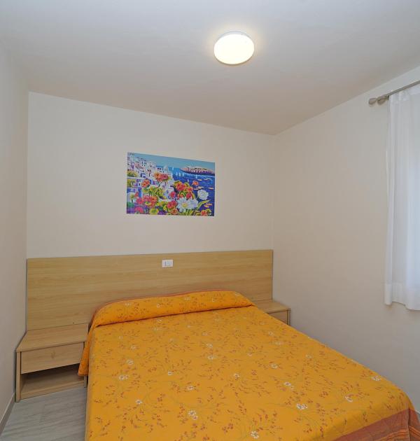Einfaches Zimmer mit Doppelbett und orangefarbener Bettdecke.
