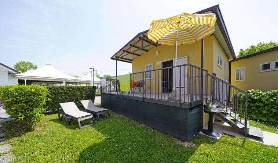Casa gialla con terrazza, ombrellone e lettini su prato verde.